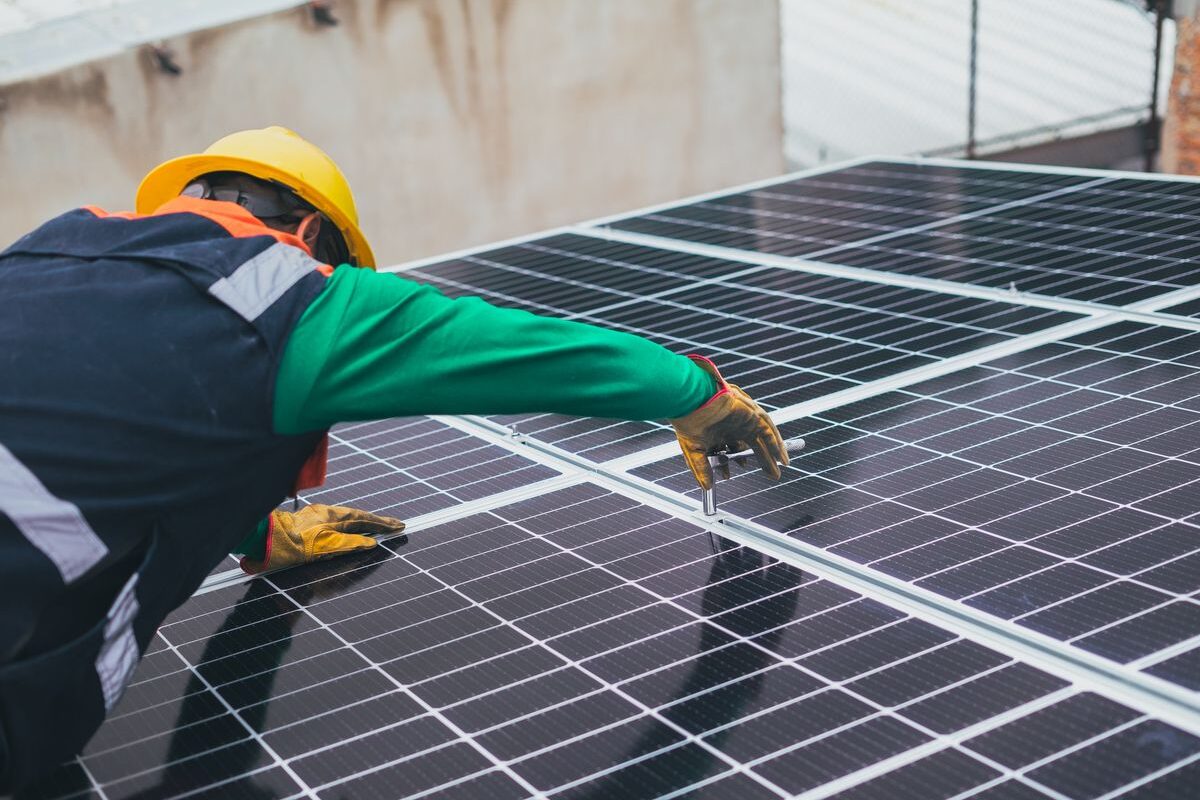 An installer in high-visibility clothing working on a rooftop covered in solar panels.